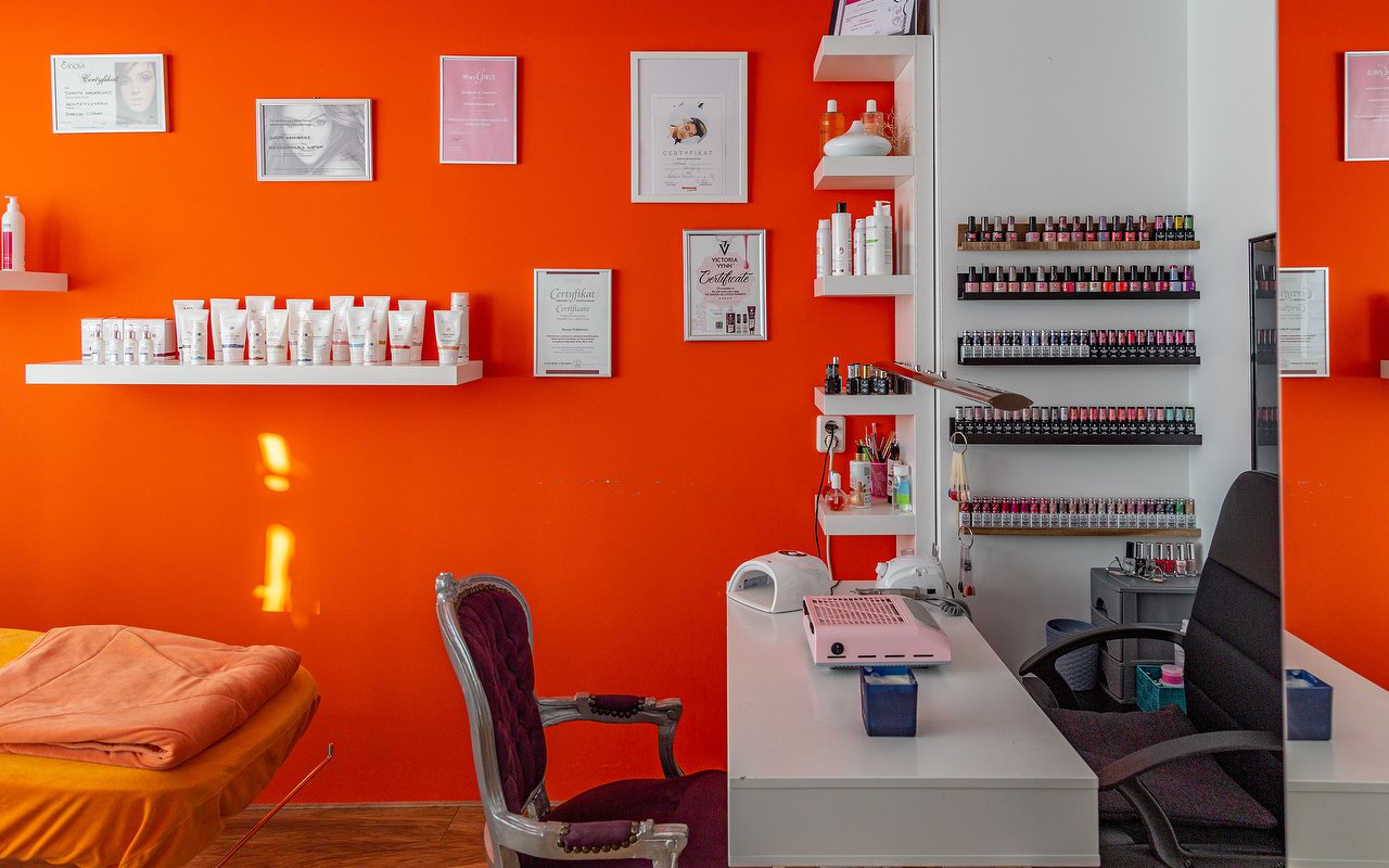 Oranje muur met planken vol producten, diploma's, een wand met gellak en de manicuretafel